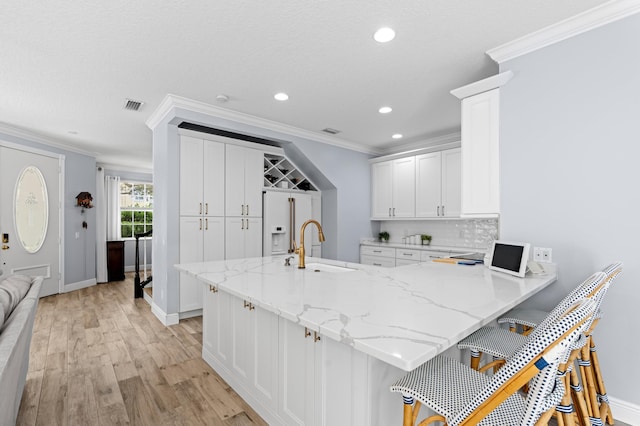240 Honeysuckle Dr, Jupiter, FL 33458 - kitchen featuring crown molding, a peninsula, white cabinets, a breakfast bar area, and light wood-style flooring