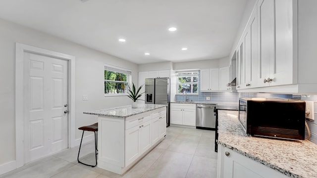 218 NE 10th St, Delray Beach, FL 33444 - kitchen with stainless steel appliances, a kitchen breakfast bar, backsplash, a kitchen island, and white cabinetry