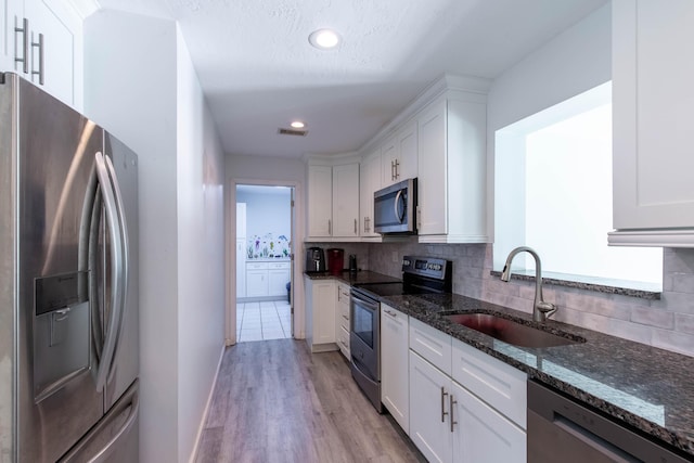12069 Easterly Ave, Palm Beach Gardens, FL 33410 - kitchen with appliances with stainless steel finishes, white cabinetry, tasteful backsplash, dark stone countertops, and light wood-style flooring