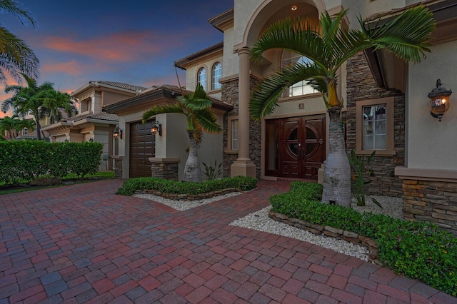718 Edgebrook Ln, West Palm Beach, FL 33411 - exterior entry at dusk with stucco siding, stone siding, and decorative driveway