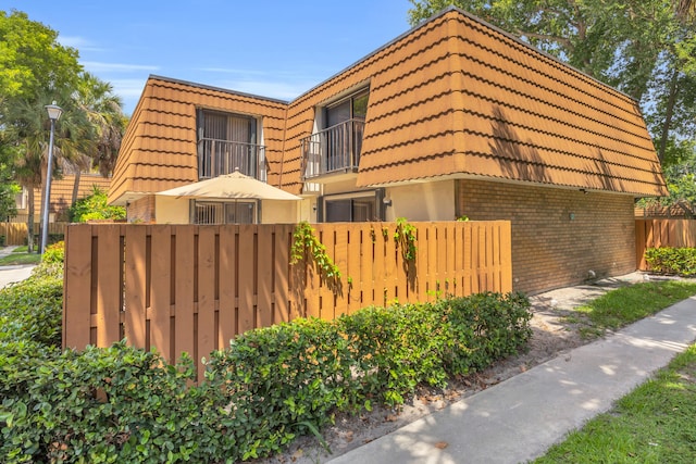 182 Charter Way, West Palm Beach, FL 33407 - view of home's exterior featuring a tile roof, mansard roof, brick siding, a balcony, and stucco siding