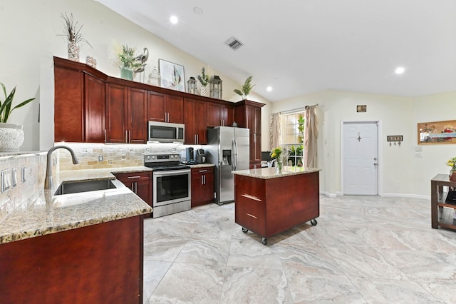 8404 Long Bay, West Palm Beach, FL 33411 - kitchen featuring appliances with stainless steel finishes, reddish brown cabinets, tasteful backsplash, a center island, and light stone counters