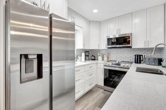 313 Saxony Unit G, Delray Beach, FL 33446 - kitchen featuring stainless steel appliances, white cabinetry, light wood-style flooring, backsplash, and recessed lighting