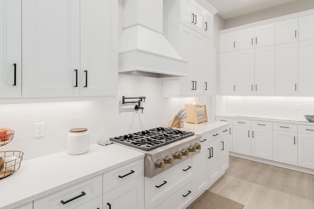 3153 SW Pond Apple St, Palm City, FL 34990 - kitchen with stainless steel gas cooktop, premium range hood, tasteful backsplash, white cabinetry, and light countertops