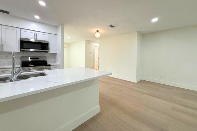 216 SE Fallon Dr, Port Saint Lucie, FL 34983 - kitchen with stainless steel appliances, light wood-style floors, recessed lighting, backsplash, and white cabinetry