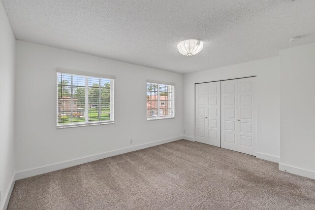 9850 Kamena Cir, Boynton Beach, FL 33436 - unfurnished bedroom featuring multiple windows, carpet, a closet, and a textured ceiling
