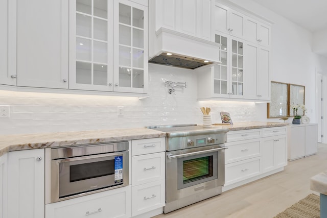 737 Nighthawk Way, North Palm Beach, FL 33408 - kitchen with appliances with stainless steel finishes, decorative backsplash, white cabinetry, glass insert cabinets, and premium range hood