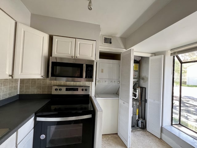 717 Gardens Dr Unit 106, Pompano Beach, FL 33069 - kitchen with stainless steel appliances, stacked washer / dryer, dark countertops, tasteful backsplash, and white cabinets