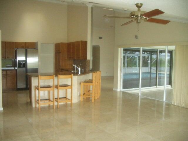 24 Dunbar Rd, Palm Beach Gardens, FL 33418 - kitchen with stainless steel fridge, ceiling fan, a towering ceiling, brown cabinets, and a peninsula