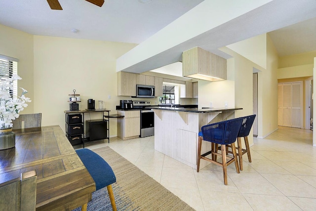 2282 NE Marlberry Ln, Jensen Beach, FL 34957 - kitchen with stainless steel appliances, a breakfast bar, light tile patterned floors, light brown cabinets, and dark countertops