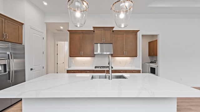 203 SE Via Sangro, Port Saint Lucie, FL 34952 - kitchen featuring stainless steel appliances, under cabinet range hood, a center island with sink, washing machine and clothes dryer, and recessed lighting