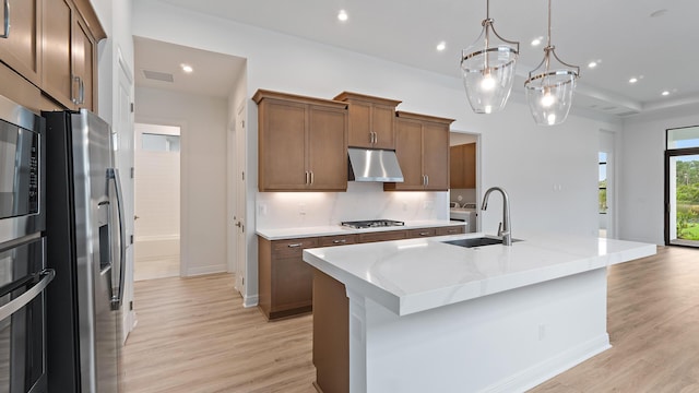 203 SE Via Sangro, Port Saint Lucie, FL 34952 - kitchen featuring under cabinet range hood, stainless steel appliances, light wood-style floors, an island with sink, and decorative light fixtures