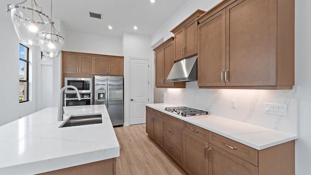 203 SE Via Sangro, Port Saint Lucie, FL 34952 - kitchen featuring appliances with stainless steel finishes, under cabinet range hood, light wood finished floors, brown cabinetry, and recessed lighting