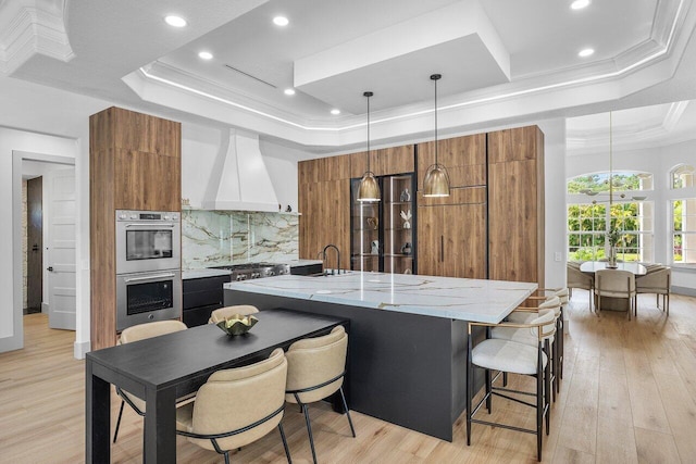 11533 Manatee Ter Unit 11533, Lake Worth, FL 33449 - kitchen with a raised ceiling, modern cabinets, stainless steel double oven, brown cabinetry, and premium range hood