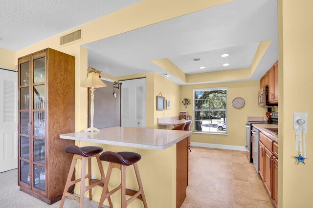 18429 SE Wood Haven Ln Unit G, Jupiter, FL 33469 - kitchen featuring brown cabinetry, a kitchen breakfast bar, stainless steel appliances, a peninsula, and light countertops