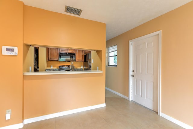 6545 SE Federal Hwy Unit 102, Stuart, FL 34997 - kitchen featuring black appliances, brown cabinets, a peninsula, light tile patterned floors, and light countertops