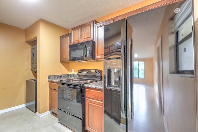 6545 SE Federal Hwy Unit 102, Stuart, FL 34997 - kitchen featuring black appliances, stacked washing machine and dryer, dark stone counters, brown cabinetry, and light tile patterned floors