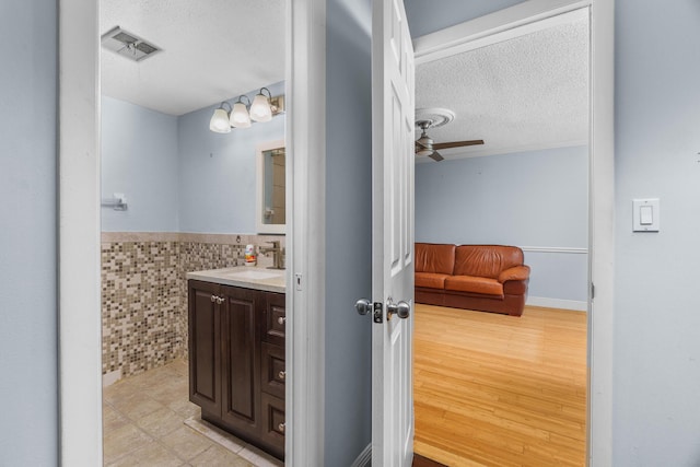 5961 NW 61st Ave Unit 203, Tamarac, FL 33319 - bathroom featuring a textured ceiling, vanity, tile walls, wainscoting, and a ceiling fan