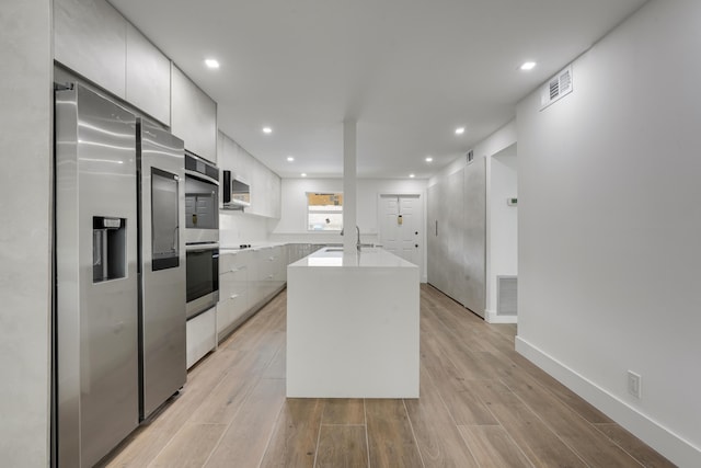 2845 SW 22nd Ave Unit 2070, Delray Beach, FL 33445 - kitchen featuring appliances with stainless steel finishes, modern cabinets, light countertops, light wood-style floors, and a center island with sink