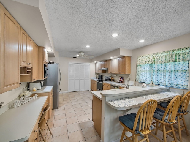 1680 SW Belgrave Ter, Stuart, FL 34997 - kitchen featuring appliances with stainless steel finishes, a kitchen bar, a textured ceiling, a ceiling fan, and light countertops