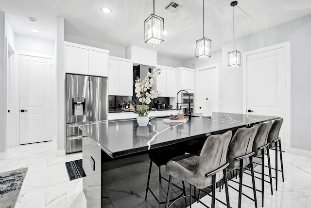 5476 NW Cambo Ct, Port Saint Lucie, FL 34986 - kitchen with stainless steel fridge with ice dispenser, light marble finish floors, white cabinets, a center island with sink, and a breakfast bar area