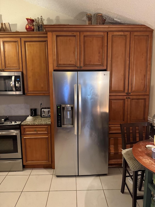 9828 Boca Gardens Trl Unit D, Boca Raton, FL 33496 - kitchen with appliances with stainless steel finishes, brown cabinetry, light tile patterned floors, a textured ceiling, and stone countertops