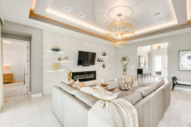 10948 SW Ivory Springs Ln, Port Saint Lucie, FL 34987 - living area featuring a tray ceiling, a glass covered fireplace, light tile patterned floors, a chandelier, and light colored carpet