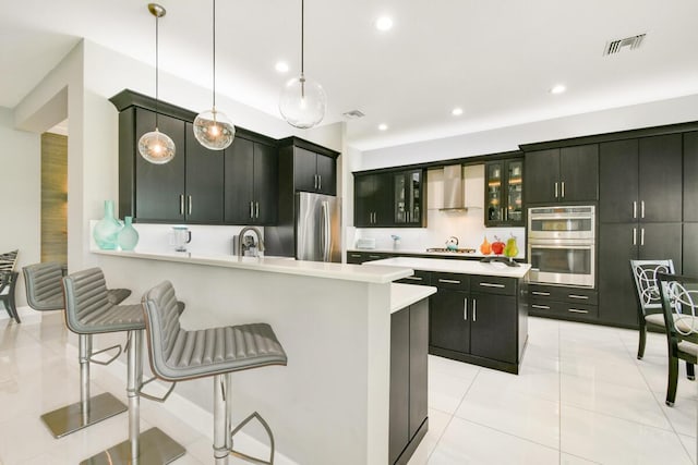 10948 SW Ivory Springs Ln, Port Saint Lucie, FL 34987 - kitchen featuring appliances with stainless steel finishes, wall chimney range hood, light countertops, a kitchen bar, and light tile patterned floors