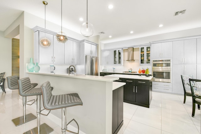 10948 SW Ivory Springs Ln, Port Saint Lucie, FL 34987 - kitchen featuring appliances with stainless steel finishes, wall chimney exhaust hood, light countertops, a kitchen breakfast bar, and a peninsula