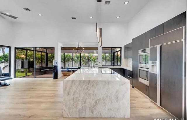 2299 NW 55th St, Boca Raton, FL 33496 - kitchen featuring stainless steel double oven, modern cabinets, paneled fridge, light wood-type flooring, and a towering ceiling