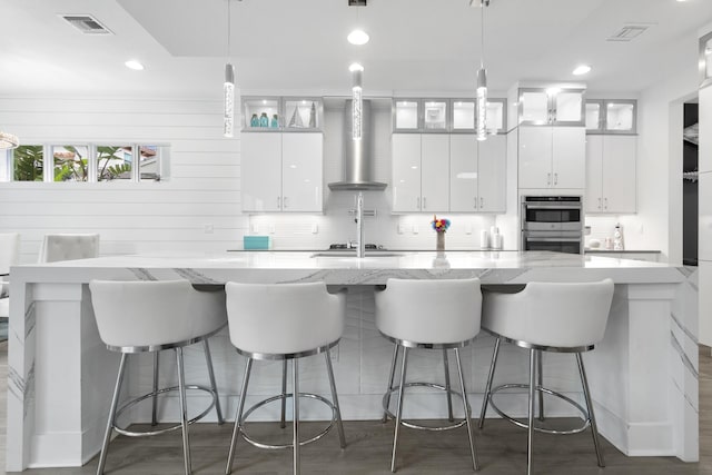 13313 Machiavelli Way, Palm Beach Gardens, FL 33418 - kitchen featuring wall chimney exhaust hood, stainless steel appliances, white cabinetry, decorative light fixtures, and a large island with sink