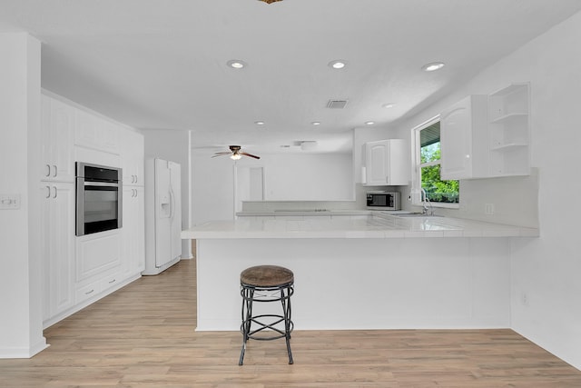 5801 SE Cable Dr, Stuart, FL 34997 - kitchen with stainless steel appliances, a peninsula, white cabinets, a breakfast bar, and light wood-type flooring
