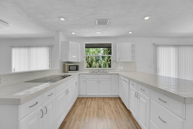 5801 SE Cable Dr, Stuart, FL 34997 - kitchen with black electric cooktop, a peninsula, dishwasher, tasteful backsplash, and light wood-type flooring