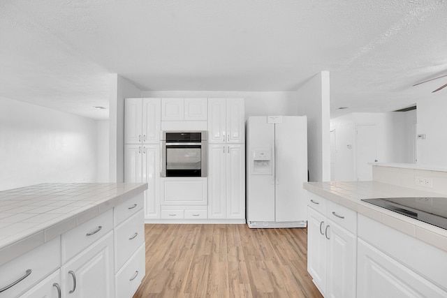 5801 SE Cable Dr, Stuart, FL 34997 - kitchen featuring white refrigerator with ice dispenser, stainless steel oven, tile countertops, white cabinets, and light wood finished floors
