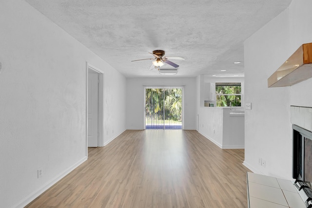 5801 SE Cable Dr, Stuart, FL 34997 - unfurnished living room featuring a fireplace, light wood-style flooring, ceiling fan, and a textured ceiling