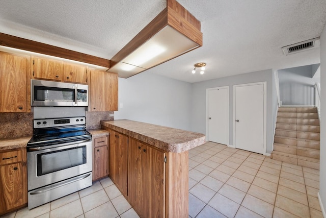 2897 SW 22nd Cir Unit 44B, Delray Beach, FL 33445 - kitchen featuring stainless steel appliances, a peninsula, light countertops, light tile patterned flooring, and a textured ceiling
