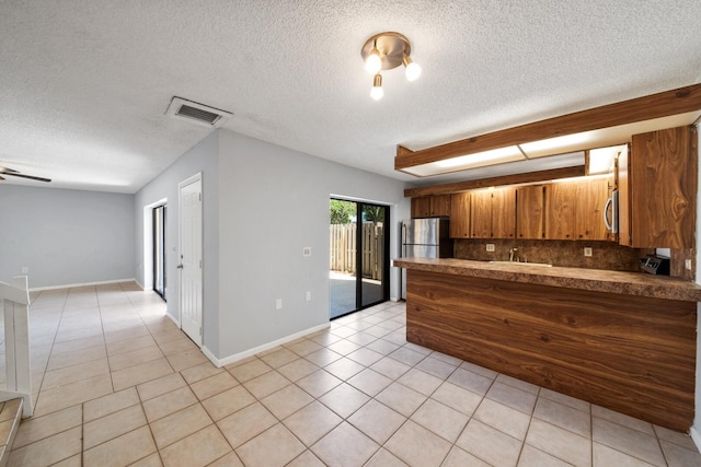 2897 SW 22nd Cir Unit 44B, Delray Beach, FL 33445 - kitchen with brown cabinets, light tile patterned floors, stainless steel appliances, tasteful backsplash, and a textured ceiling