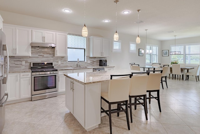 649 SE Monteiro Dr, Port Saint Lucie, FL 34984 - kitchen featuring stainless steel appliances, under cabinet range hood, decorative backsplash, a center island, and white cabinets