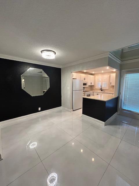 808 SE 7th St Unit 107, Deerfield Beach, FL 33441 - kitchen with white appliances, crown molding, light countertops, a peninsula, and light tile patterned flooring