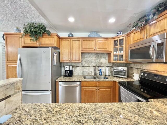 188 Upminster I Unit 188, Deerfield Beach, FL 33442 - kitchen with appliances with stainless steel finishes, light stone counters, glass insert cabinets, decorative backsplash, and recessed lighting