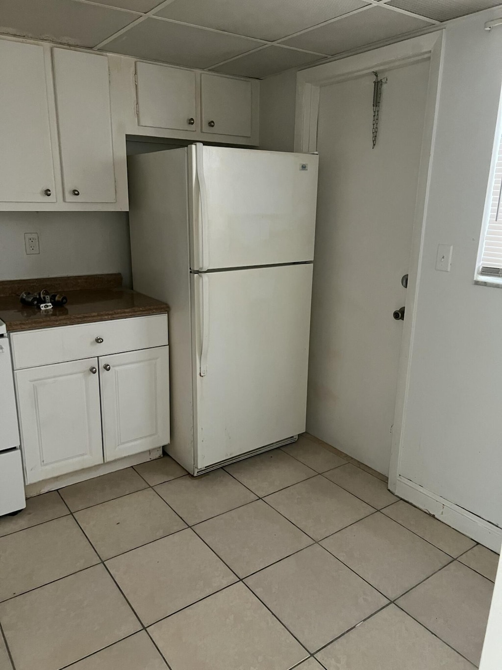 1300 NW 43rd Ter Unit 104, Lauderhill, FL 33313 - kitchen featuring freestanding refrigerator, dark countertops, white cabinetry, light tile patterned flooring, and a paneled ceiling