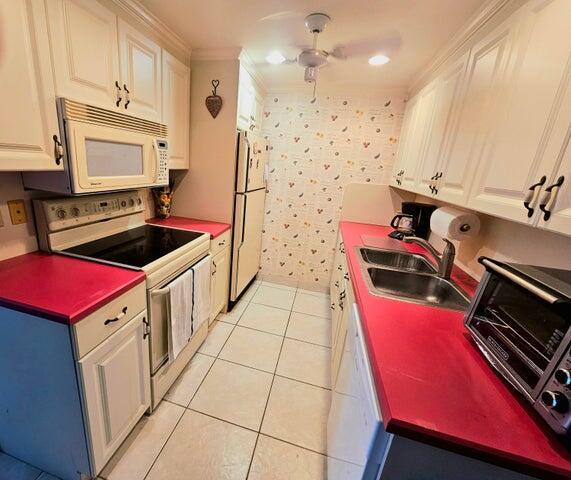 4074 Cornwall D 4074, Boca Raton, FL 33434 - kitchen with white appliances, a ceiling fan, light tile patterned flooring, crown molding, and white cabinets
