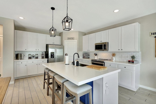 650 NE Waters Edge Ln, Port Saint Lucie, FL 34983 - kitchen featuring stainless steel appliances, backsplash, wood finish floors, white cabinetry, and a kitchen island with sink