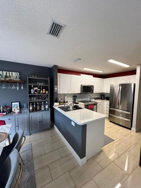 9815 Watermill Cir Unit B, Boynton Beach, FL 33437 - kitchen with appliances with stainless steel finishes, a peninsula, white cabinetry, a textured ceiling, and light countertops