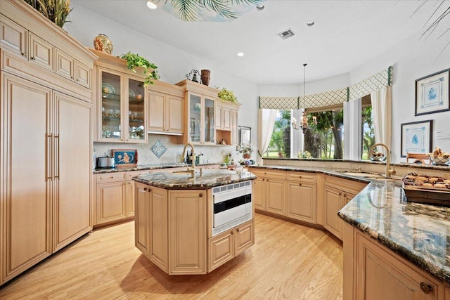 8571 Egret Lakes Ln, West Palm Beach, FL 33412 - kitchen with paneled refrigerator, light wood-type flooring, dark stone counters, tasteful backsplash, and glass insert cabinets
