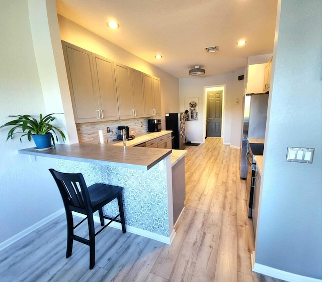 2247 SW Cape Cod Dr, Port Saint Lucie, FL 34953 - kitchen with light wood-type flooring, tasteful backsplash, a breakfast bar area, a peninsula, and freestanding refrigerator
