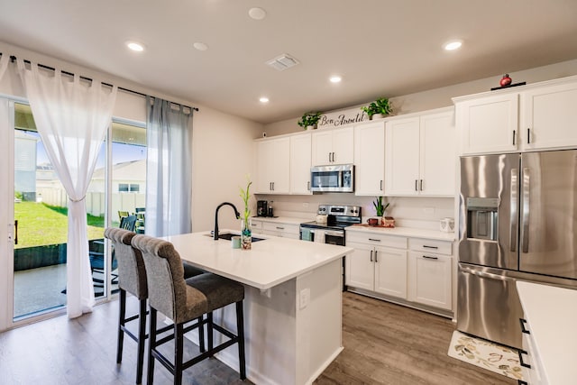 1123 Sugarwood St, Davenport, FL 33837 - kitchen with appliances with stainless steel finishes, wood finished floors, a center island with sink, a breakfast bar, and white cabinets