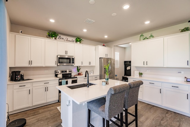 1123 Sugarwood St, Davenport, FL 33837 - kitchen featuring appliances with stainless steel finishes, wood finished floors, white cabinets, a center island with sink, and recessed lighting