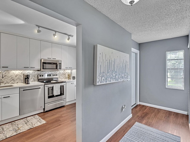 9199 Pecky Cypress Ln Unit 7H, Boca Raton, FL 33428 - kitchen featuring appliances with stainless steel finishes, backsplash, light wood-type flooring, light countertops, and rail lighting