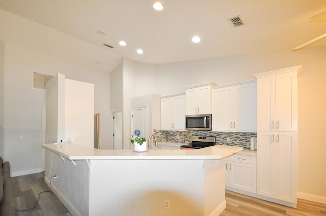 6771 NW Daffodil Ln, Port Saint Lucie, FL 34983 - kitchen featuring stainless steel appliances, tasteful backsplash, light wood finished floors, white cabinetry, and vaulted ceiling